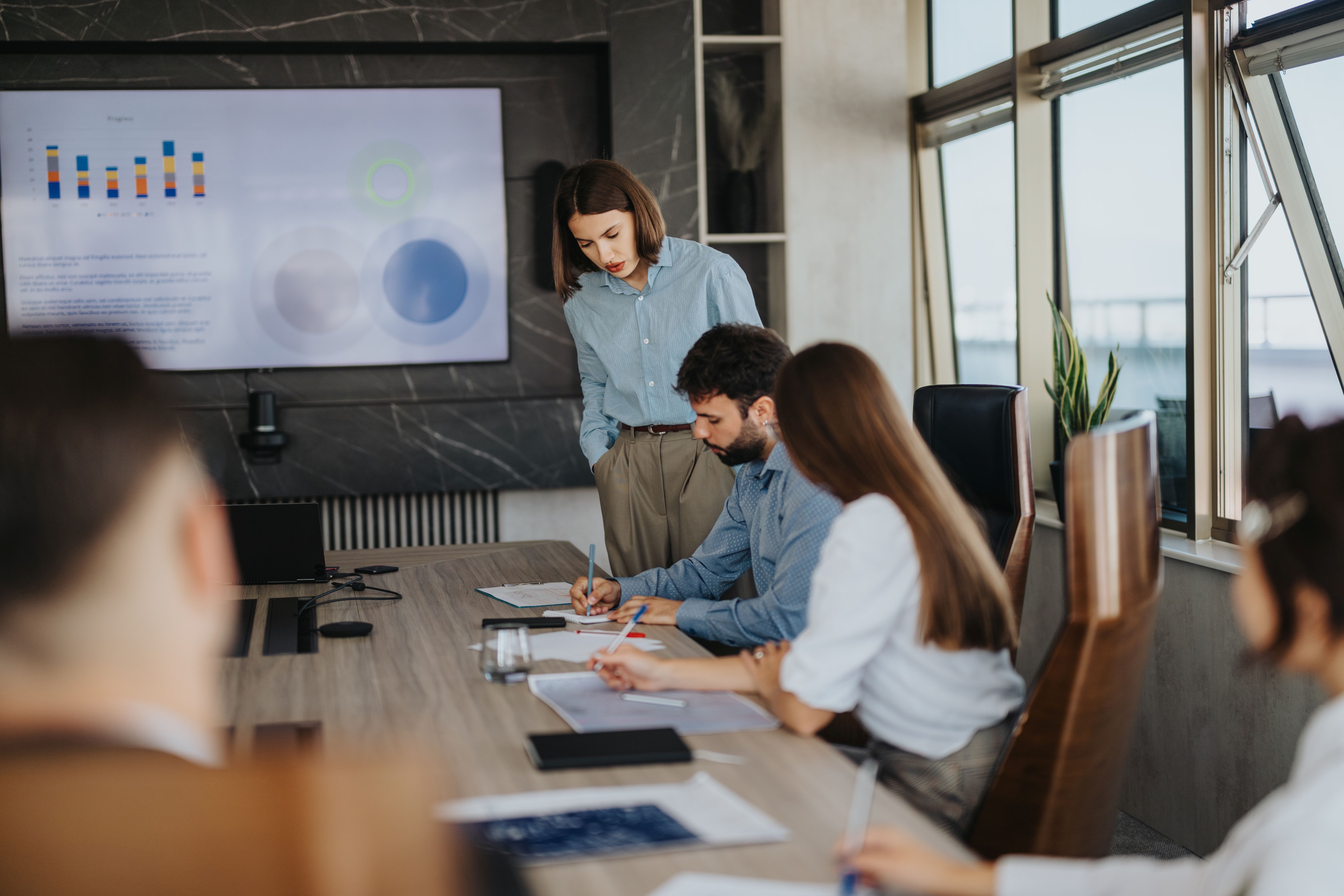 Moderner Besprechungsraum mit Berufstätigen im Smart-Casual-Look, die eine Strategiepräsentation mit Säulendiagrammen diskutieren.