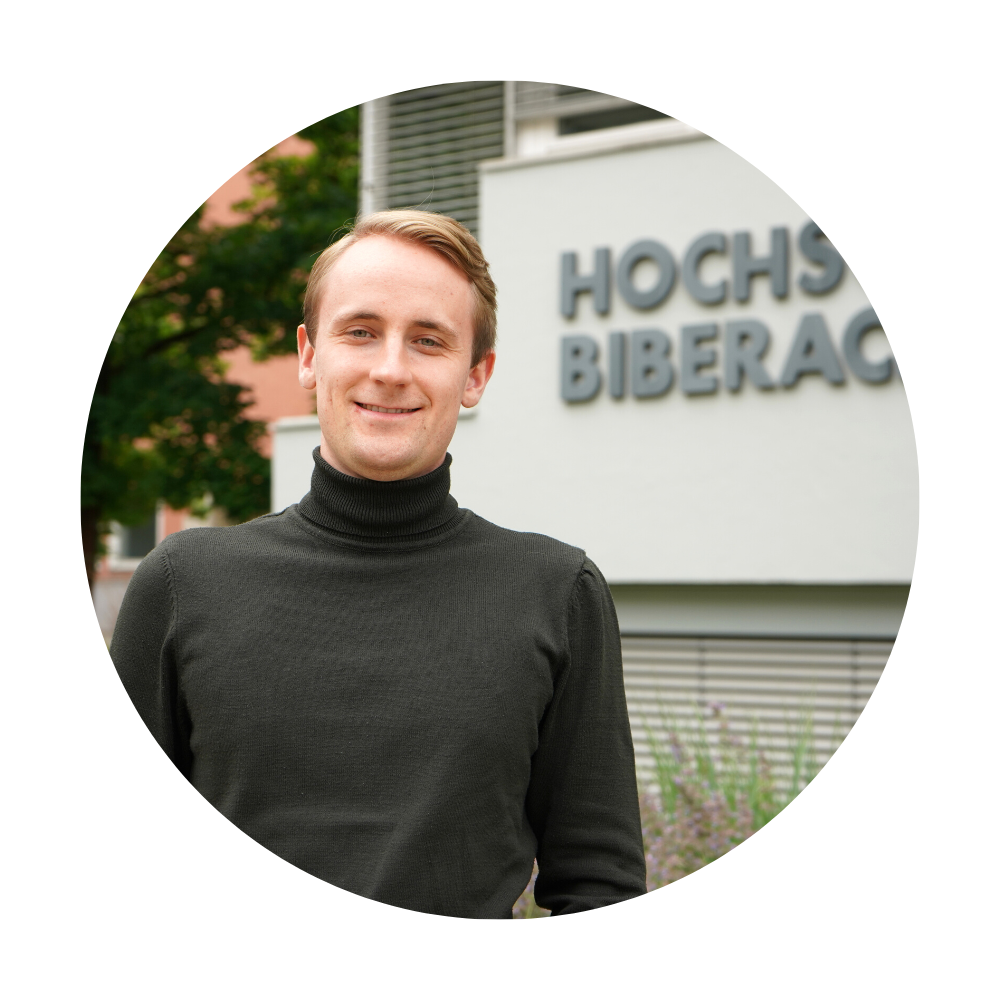 Junger Mann mit kurzen blonden Haaren und Rollkragenpullover vor Hochschulgebäude