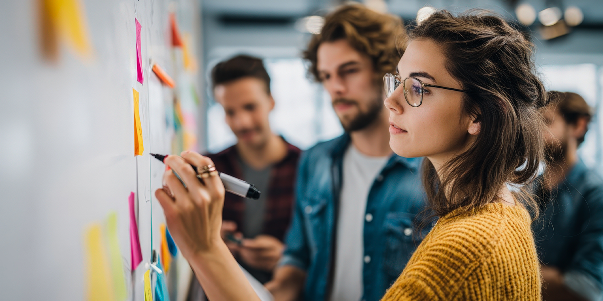 Studierende im legerem casual Look stehen mit Stift vor einem Whiteboard mit vielen bunten Post-its