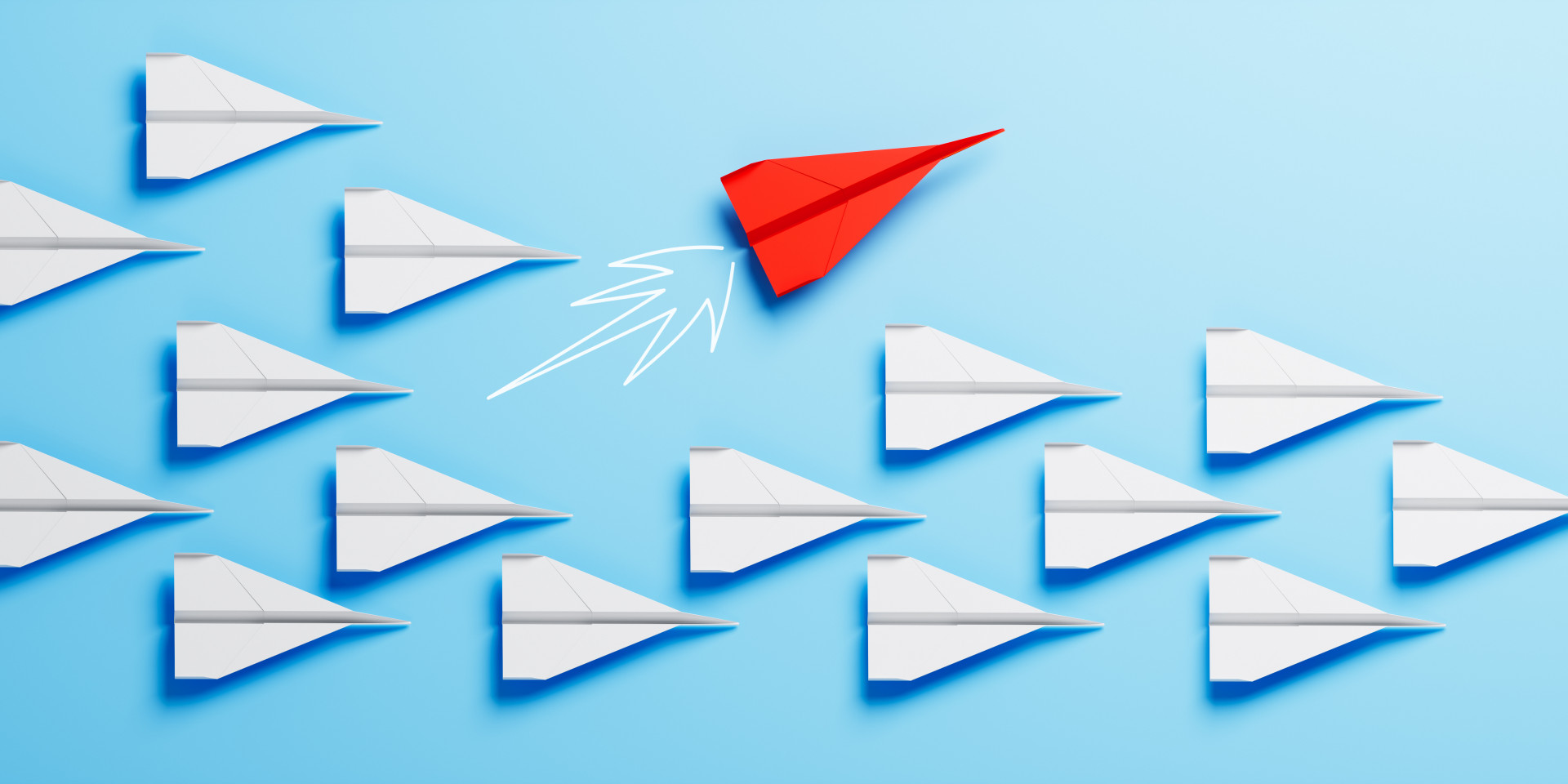Das Bild zeigt viele weiße Papierflieger, die alle in dieselbe Richtung fliegen. Zwischen ihnen befindet sich ein einzelner roter Papierflieger, der in eine andere Richtung fliegt als die weißen. Der Hintergrund ist in einem kräftigen Türkis gehalten, wodurch die Papierflieger besonders gut zur Geltung kommen. Das Bild vermittelt den Eindruck von Individualität und Anderssein inmitten einer Gruppe.