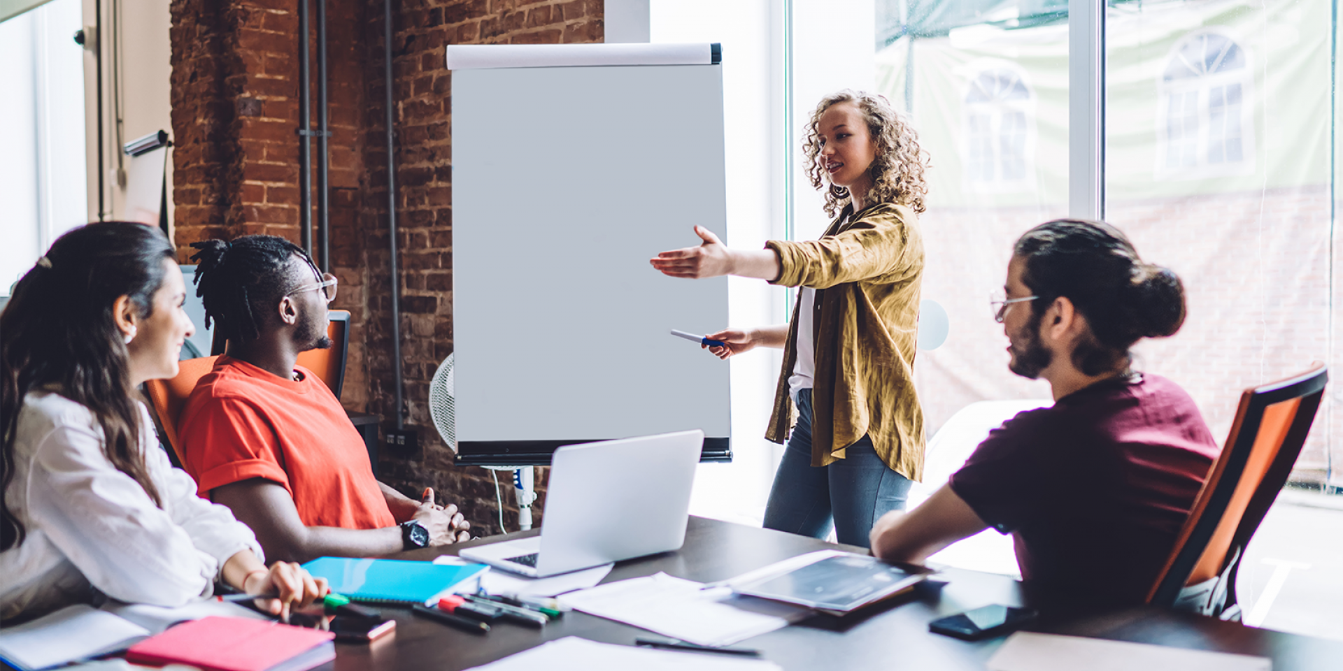 Vier Studierende unterschiedlicher Nationalitäten sitzen in einem modernen Besprechungsraum mit Flipchart und diskutieren