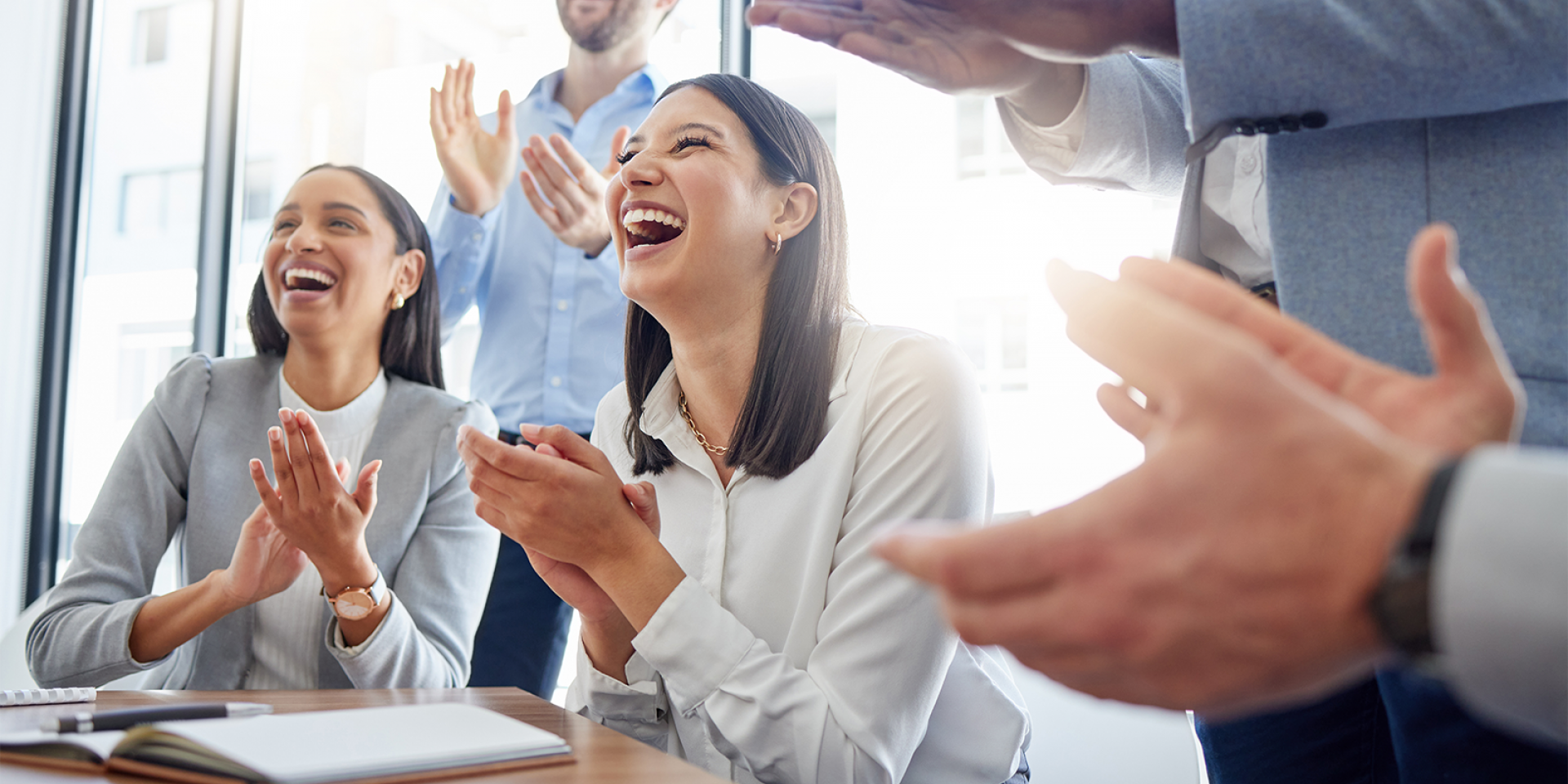 Eine Gruppe von gut gelaunten Mitarbeitenden im Business Look applaudieren in einem Meeting und unterstützen sich gegenseitig.