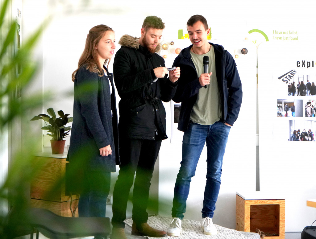 Drei Personen stehen bei einem Pitch auf einer Bühne