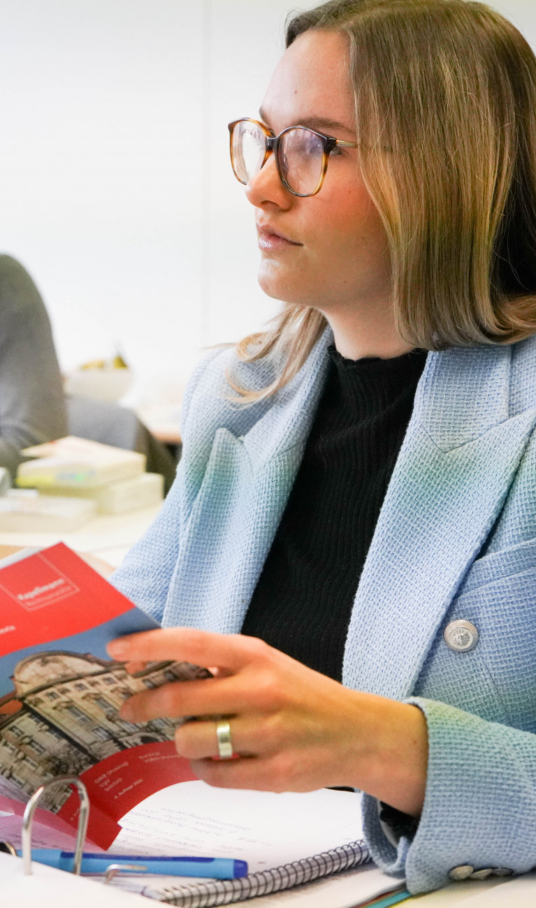 Junge Frau mit blauem Blazer sitzt in Vorlesung und hält Buch in der Hand