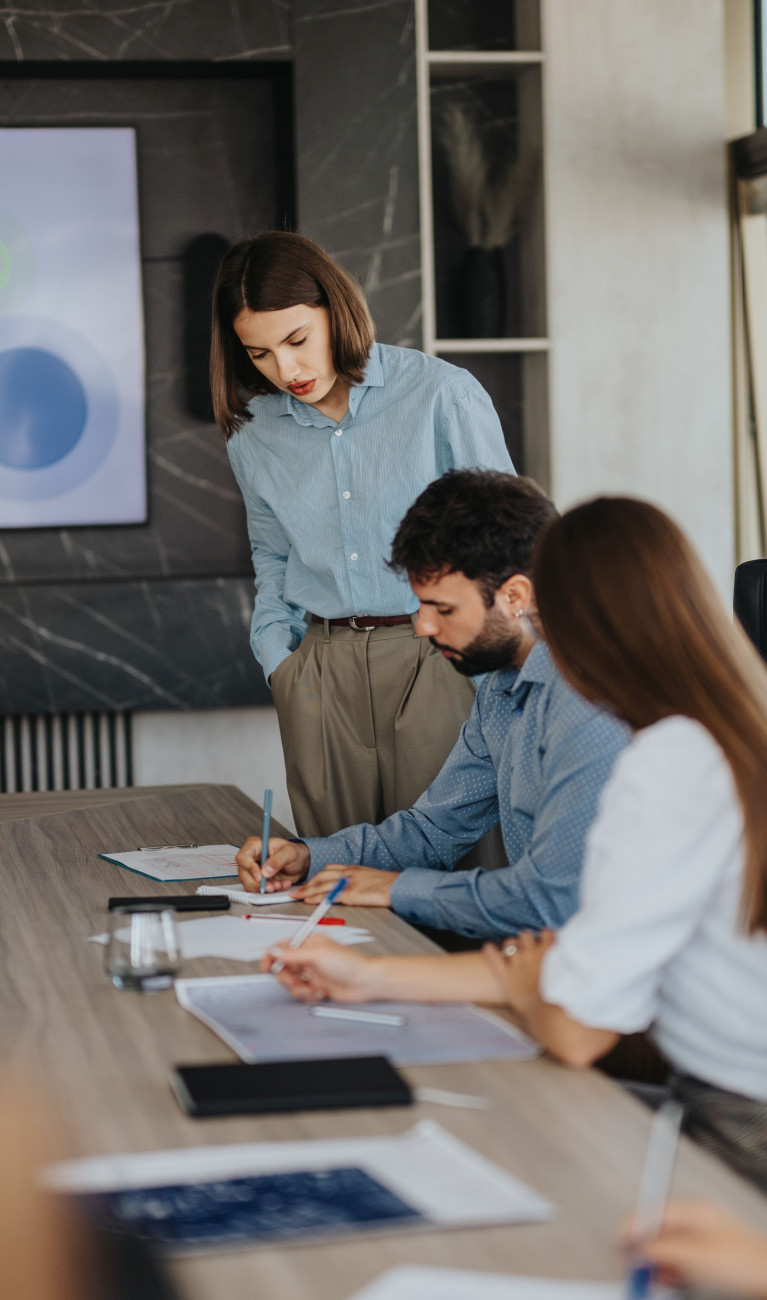 Moderner Besprechungsraum mit Berufstätigen im Smart-Casual-Look, die eine Strategiepräsentation mit Säulendiagrammen diskutieren.