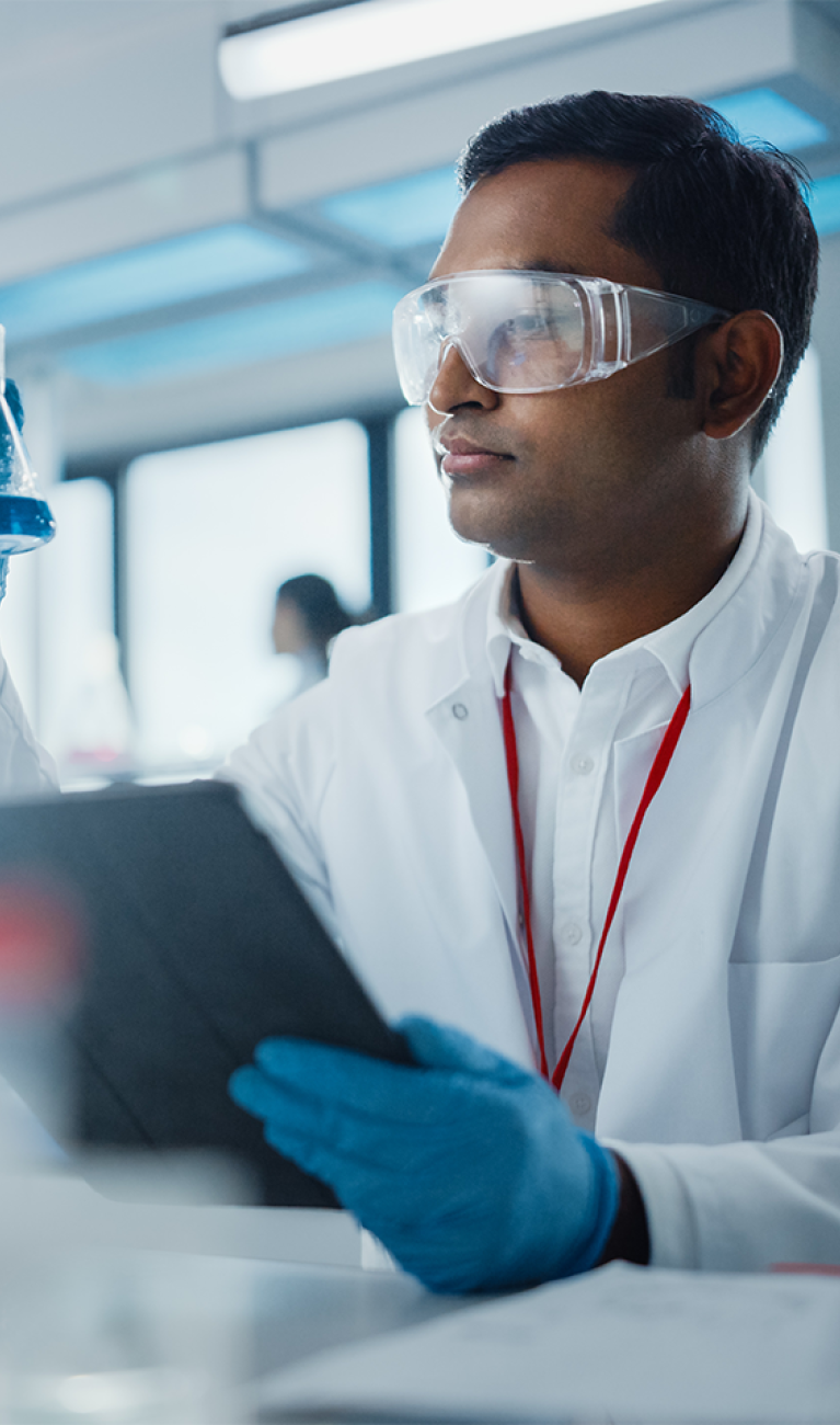 Männlicher Wissenschaftlers analysiert flüssige Biochemikalien in einem Erlenmeyerkolben und verwendet ein digitales Tablet in einem modernen Biotechnologielabor.