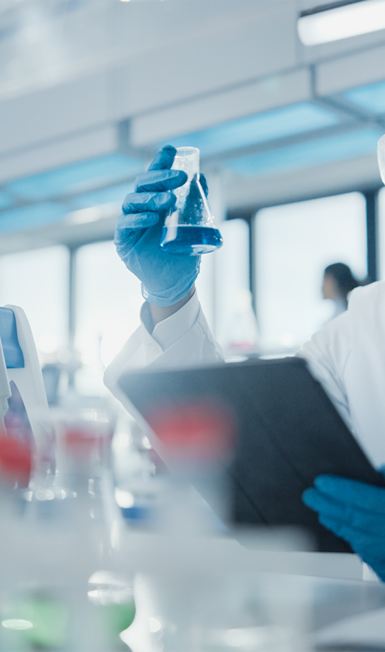 Männlicher Wissenschaftlers analysiert flüssige Biochemikalien in einem Erlenmeyerkolben und verwendet ein digitales Tablet in einem modernen Biotechnologielabor.