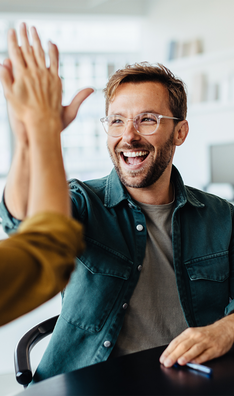 Junge gut gelaunte Leute im Casual Look feiern Erfolg im Büro und klatschen sich ab mit High Five