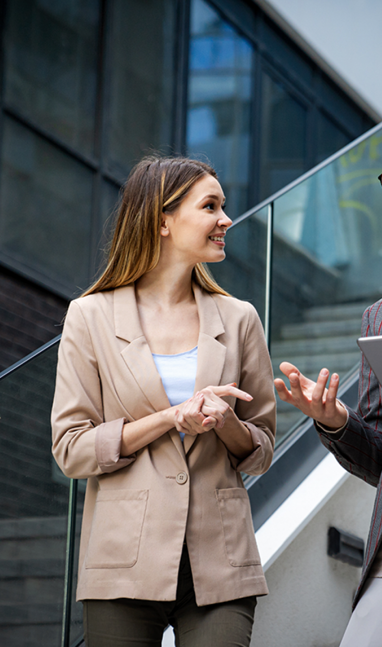 Eine Frau und ein Mann mit Tablet in der Hand, beide im Business Look, stehen auf einer Treppe in einem modernen Unternehmen und unterhalten sich,