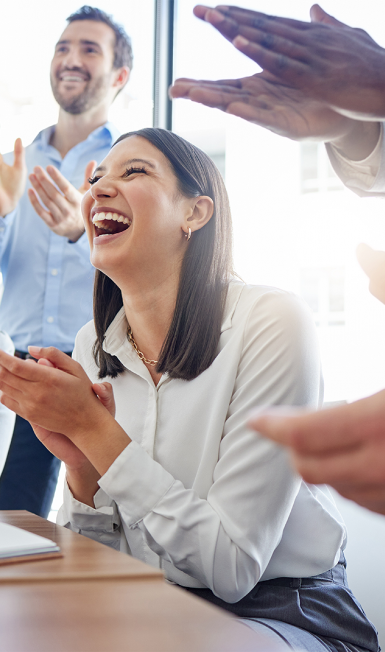 Eine Gruppe von gut gelaunten Mitarbeitenden im Business Look applaudieren in einem Meeting und unterstützen sich gegenseitig.