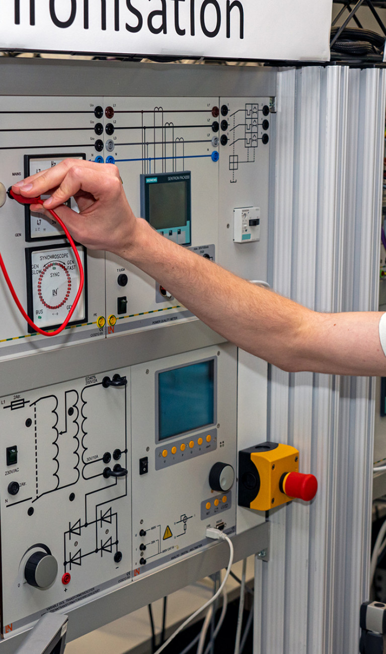 Studierender Jens Hagmeyer steht vor Modell Netzsynchronisation im Labor für Elektrische Systeme