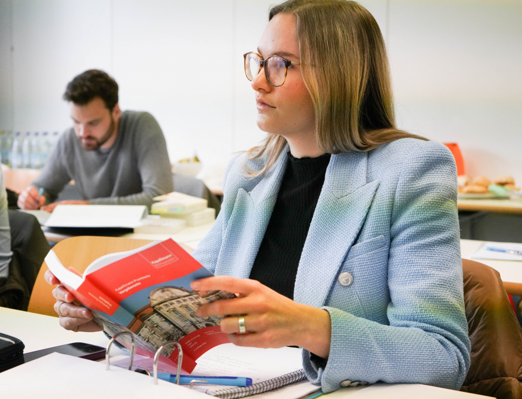 Junge Frau mit blauem Blazer sitzt in Vorlesung und hält Buch in der Hand
